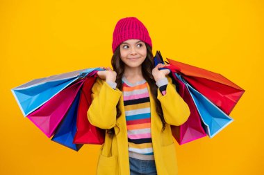Sarı arka planda alışveriş torbaları olan güzel moda kızı. Sonbahar alışverişi. Alışveriş çantalı çocuk. Mutlu ergen, pozitif ve gülümseyen duygular
