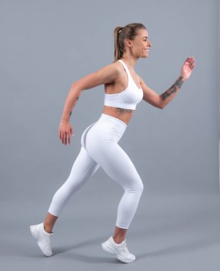 Genç sporcu kadın koşucu koşmadan önce bacaklarını esnetiyor. Gri arka planda sportif kadın koşucu. Dinamik hareket. Spor ve sağlıklı yaşam tarzı