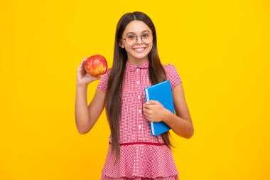 Okula dönelim. Çantalı liseli kız. Elma ve kitap tutuyor. Öğrenmeye hazır. İzole edilmiş sarı arka planda okul çocukları