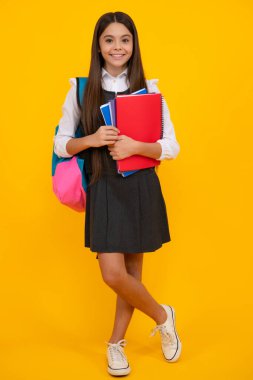 School teenage girl with school bag backpack hold book on yellow isolated studio background. Children school and education concept