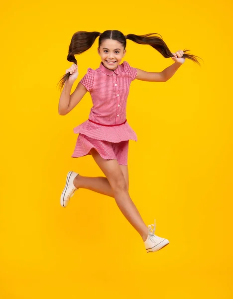 Excited teenager. Full length funny teenager kid jump enjoy rejoice win isolated on yellow background. Small child girl in dress jumping