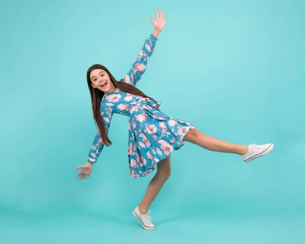 Excited teenager, amazed and cheerful emotions. Full length cheerful teenager kid jump enjoy rejoice win isolated on blue background. Small child girl in summer dress jumping
