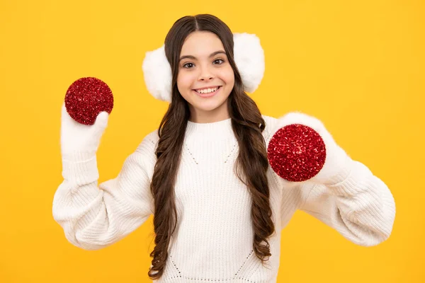 Merry christmas and happy New year. Portrait of happy teenager child wears sweater and knitted gloves on yellow isolated background. Kid in winter clothes. Teen girl with decorative christmas ball