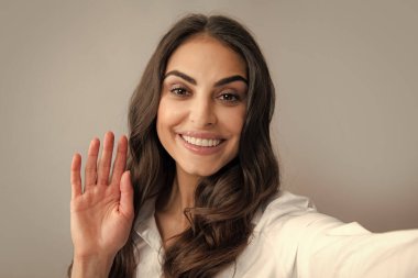 Gri arka planda izole edilmiş heyecanlı genç bir kadın fotoğraf makinesiyle selfie çekiyor.