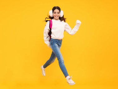 Schoolgirl child student with backpack and warn hat, isolated yellow background. Learning and knowledge education concept