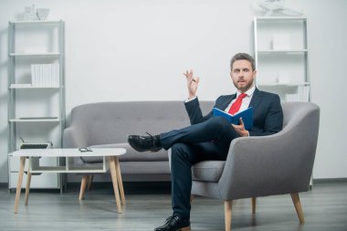 Takım elbiseli olgun iş adamı ofiste oturup kitap okuyor..