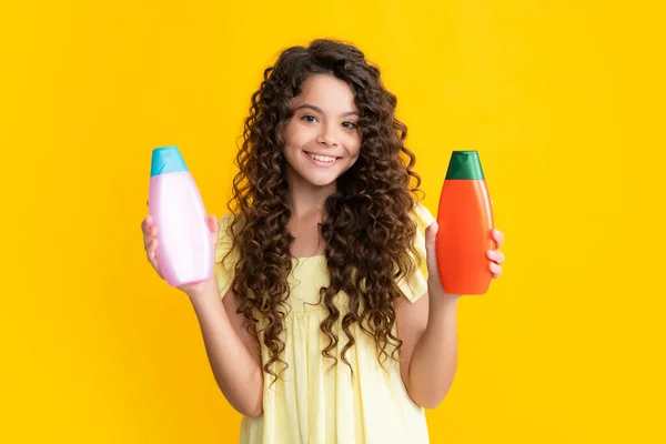 Happy teenager, portrait of child girl with bottle shampoo conditioners or shower gel. Kids hair care. Hair cosmetic product, shampoo bottle. Smiling girl