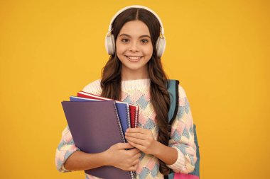 Liseli kız, kulaklıklı ergen öğrenci sarı izole stüdyo geçmişiyle ilgili kitaplar tutuyor. Okul ve müzik eğitimi kavramı