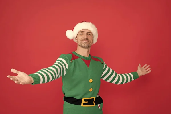 happy man in elf costume. xmas guy in santa claus hat on red background. happy new year. merry christmas. welcome gesture.