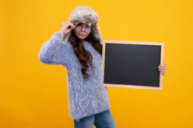 Kara tahtalı, kışlık şapkalı küçük bir kız. Liseli kız fotokopi odası ve okul satışı için karatahta tutuyor.