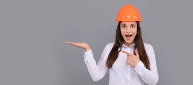 İzole edilmiş bir yüz portresi, taklit alanı olan bir afiş. Koruyucu miğferli, tişörtlü, parmakla işaret eden ve fotokopi alanı ve reklam sunan hayret verici kadın.