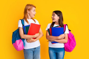 Okul, öğrenme ve eğitim konsepti. Okul çantalı ve kitapları öğrenmeye hazır anne-kız okul kızları. Okula dönelim. Anne ve çocuk izole edilmiş sarı stüdyo geçmişinde