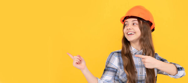 Renovation child, happy teen girl in helmet and checkered shirt pointing finger on copy space, advert. Child in hard hat horizontal poster design. Banner header, copy space