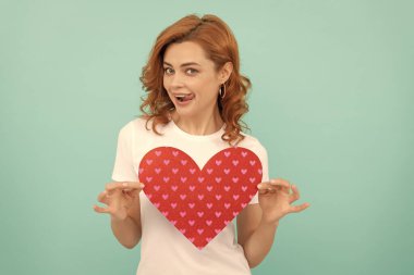 Neşeli kızıl saçlı bayan mavi arka planda kırmızı kalbi tut..