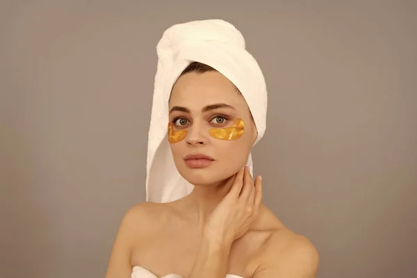 shine future. skincare. facial collagen cosmetic. moisturizing skin. cosmetology. young woman in terry towel use patch. beauty day in spa. applying golden anti-fatigue mask. girl reduce eye bags.