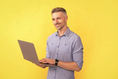 Mutlu olgun bir adam internette çalışıyor sarı arka planda bilgisayar, iş.