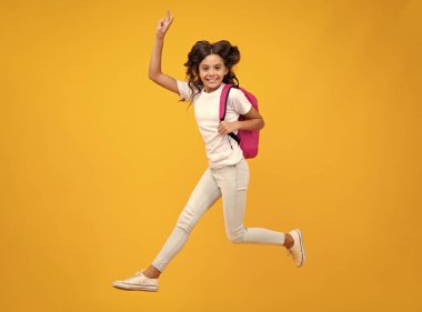Şaşırmış genç kız. Okul üniformalı okul çantalı kız. Okul çocuğu, genç öğrenci sırt çantasını sarı izole edilmiş arka planda tutuyor. Koş ve atla. Heyecanlı bir ifade, neşeli ve mutlu.