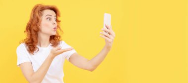 Kız, el öpme hareketini kameraya, telefon sarısına ve mobil cihaza yapıyor. İzole edilmiş yüz portresi, taklit alanı olan pankart