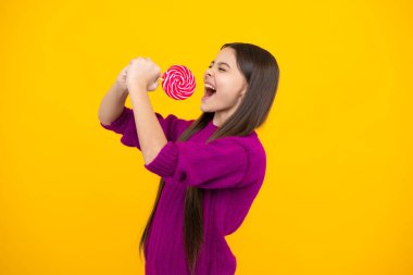 Heyecanlı bir yüz. Hippi ergen kız lolipopu yalıyor. Şeker, şeker ve şekerleme. Çocuk lolipop şekeri yiyor. Şaşırtıcı bir ifade, neşeli ve mutlu.