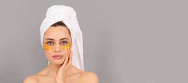 Güzel yüzlü kadın, yüz portresi. Terry havlusu olan genç bir kadın cilt için altın göz bandı kullanır. Güzel kadın, izole edilmiş yüz portresi, taklit alanı olan pankart.