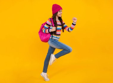 Sonbahar okulu tatili. Okula dönelim. Sonbahar kıyafetleri içinde sarı izole edilmiş stüdyo arka planında genç bir kız öğrenci. Atla ve kaç, zıplayan çocuklar.