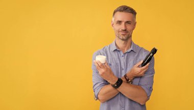 traş sonrası. Elinde elektrikli tıraş makinesi ve krem tutan bir adam. Gri saçlı adam elektrikli jilet sunuyor. Saç bakımı ve tıraş. Kişisel bakım ve cilt bakımı. Erkek güzelliği. Berber dükkanı. Boşluğu kopyala.