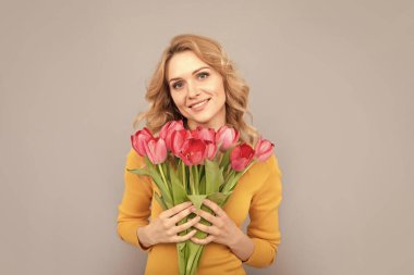 Gülümseyen bayan, bahar tatili için çiçekleri gri arka planda tut.