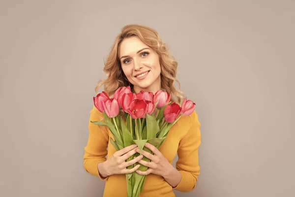 smiling lady hold flowers for spring holiday on grey background.
