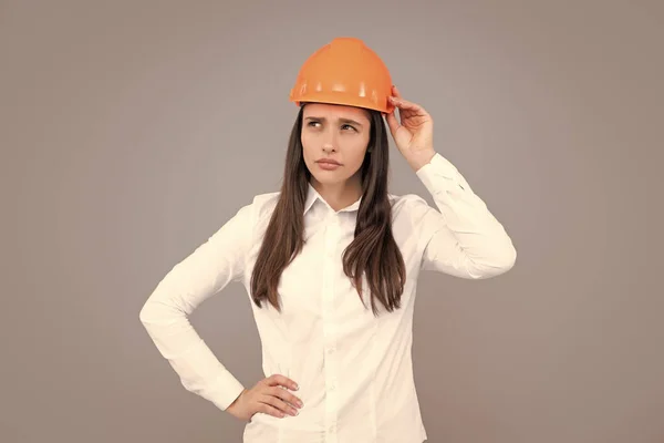 Funny woman in helmet on gray background. Architect businesswoman in helmet thinking, young caucasian female in work as constructor engineer