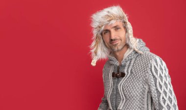 Kırmızı arka planda beyaz kazaklı ve kulaklı adam, kış modası..