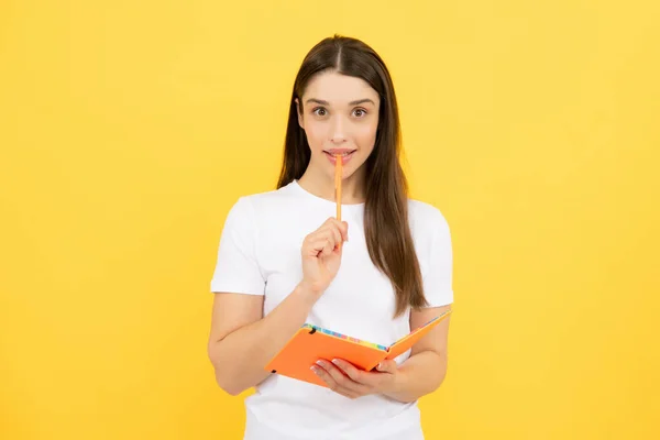 Thinking student. Young student girl in casual clothes, isolated on yellow background studio portrait. Hold notebooks. Cheerful young attractive student woman