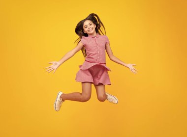 Tam boy esmer kız ergen atlama koşusu. Acele et, sarı arka plandaki stüdyoda izole ol.