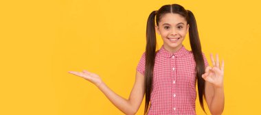 Mutlu çocuk ürününü sarı arka plan fotokopi programında sunuyor. Tamam, reklam. Çocuk yüzü, yatay poster, izole edilmiş genç kız portresi, fotokopi alanı olan pankart