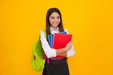 School teenage girl with school bag backpack hold book on yellow isolated studio background. Children school and education concept