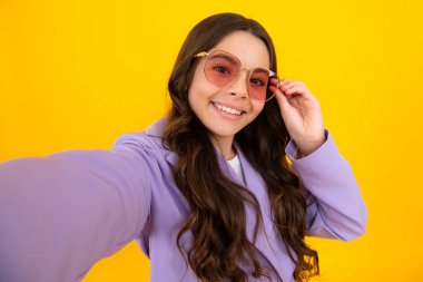 Trendy beautiful teenage model making selfie posing on yellow studio background. Teen fashion