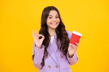 Bir fincan cappuccino kahvesi ya da çayı götüren genç kız. Sarı arka planda yemek fincanı olan çocuk, sabah içeceği. Mutlu yüz, pozitif ve gülümseyen genç kız duyguları