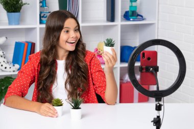 Genç blogcu video çekiyor, çocuk vlogcusu nüfuzlu kayıt içeriği. Çocuk blogcu cep telefonundaki videoyu halka lambası, video ışıkları veya evdeki video bloğu kullanarak kaydeder. Mutlu gülümseyen kız