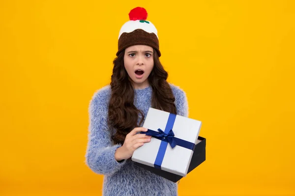 Child with gift present box on isolated yellow background. Presents for birthday, Valentines day, New Year or Christmas. Shocked amazed face, surprised emotions of young teenager girl