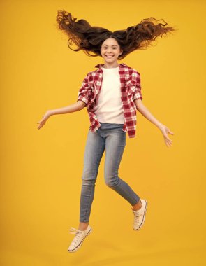 Tam boy esmer kız ergen atlama koşusu git ve sarı arka plandaki stüdyoya saklan. Çılgın hareketli saçları olan genç bir yüz.