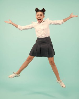 Heyecanlı bir yüz. Şaşırtıcı bir ifade, neşeli ve mutlu. Mavi arka planda izole edilmiş neşeli genç çocuk atlayışının keyfini çıkar. Yazlık elbiseli küçük bir kız çocuğu.