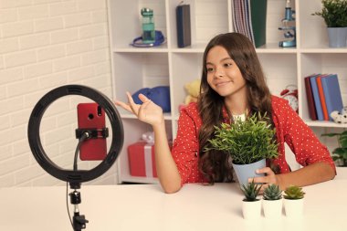 Genç blogcu video çekiyor, çocuk vlogcusu nüfuzlu kayıt içeriği. Çocuk blogcu cep telefonundaki videoyu halka lambası, video ışıkları veya evdeki video bloğu kullanarak kaydeder. Mutlu gülümseyen kız