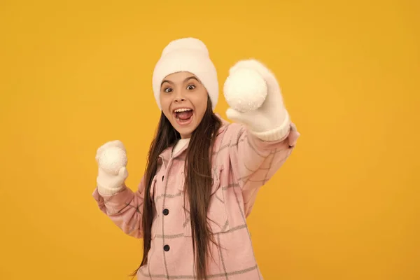 雪玉をやってる 冬の活動 帽子の子供を驚かせた 黄色の背景に装飾ボールを持つミトンの10代の女の子 クリスマスの飾りだ 暖かい服を着た子供は — ストック写真