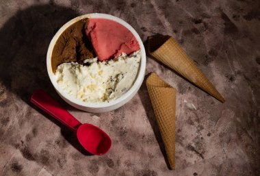 Farklı aromalı bir kilo dondurma, iki koni ve dondurma servisi için bir kaşık. Her şey masaya yaslanıyor.