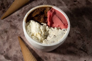 Farklı tatlara sahip bir kilo dondurma ve iki külah dondurma. Her şey bir masada desteklenir. Dondurmanın tadı çilek, limon, krema ve beyaz çikolatadır..