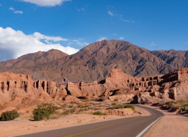 Kırmızı, turuncu, kahverengi dağların arasında bir rota. Yol kıvrımları. Farklı şekillere sahip dağlarla manzarayı ve çift sarı çizgili asfalt yolu görebilirsiniz..