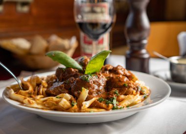 Restoran masasında beyaz tabakta kırmızı soslu bir sürü şehriye. Bir bardak şarap ve çeşitli ekmeklerle birlikte bir de biber kabı var..