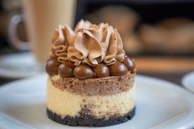 Bireysel yuvarlak çikolata, krema ve karamel kremalı keke yakın çekim. Arkanızda bir kapuçino bardağı görebilirsiniz..