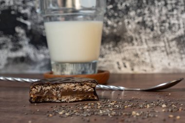 one half of chocolate cookie, filled with caramel with a glass cup of milk.on a wooden table and with a black and white textured background