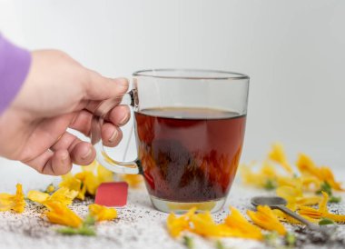 a hand holding a glass transparent cup with tea. yellow petals are observed around