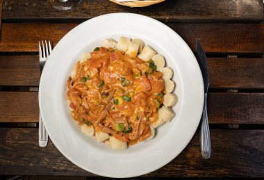 a wooden table with a dish with gnocchi with red sauce. you can see the fork and knife resting on the table.
